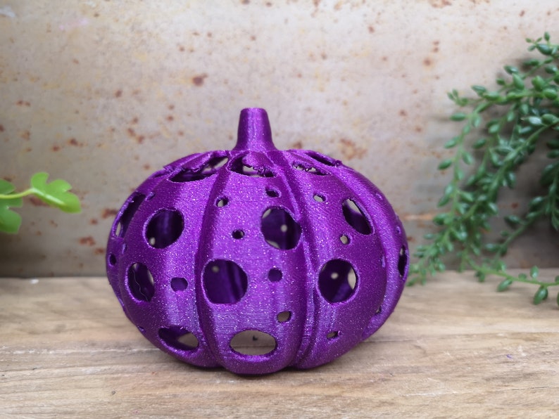 May include: A purple, 3D printed pumpkin with a hollow, dotted design. The pumpkin is made of a sparkly, textured material.