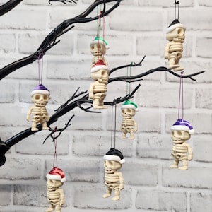 May include: Seven skeleton ornaments hanging from a tree branch. Each skeleton is wearing a different coloured Santa hat. The hats are green, red, purple, and white.