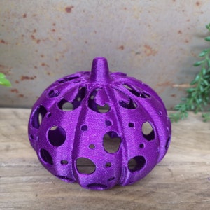 May include: A purple, glittery, hollow pumpkin with a decorative design. The pumpkin is made of plastic and has a round shape.