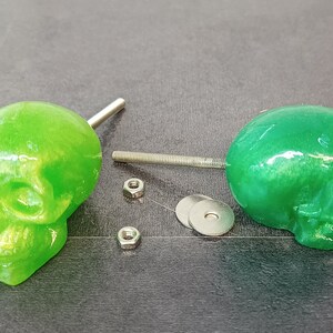 May include: Two green skull-shaped drawer pulls with silver metal screws and washers.