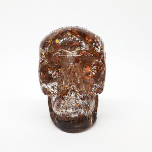 May include: A brown resin skull with gold and silver flecks embedded inside. The skull is a decorative object.