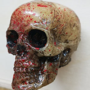 May include: A white skull with red paint splatters. The skull is made of plastic and has a detailed design.