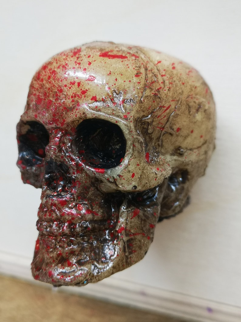 May include: A white skull with red paint splatters. The skull is made of plastic and has a detailed design.