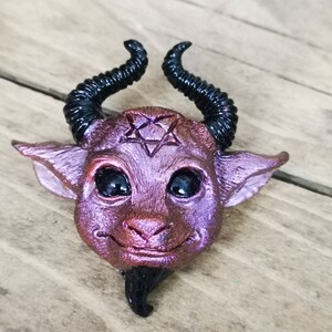 Puede incluir: Una peque&ntilde;a figurita esculpida de un demonio, de color morado y negro, con cuernos, un pentagrama en la frente y una peque&ntilde;a barba.