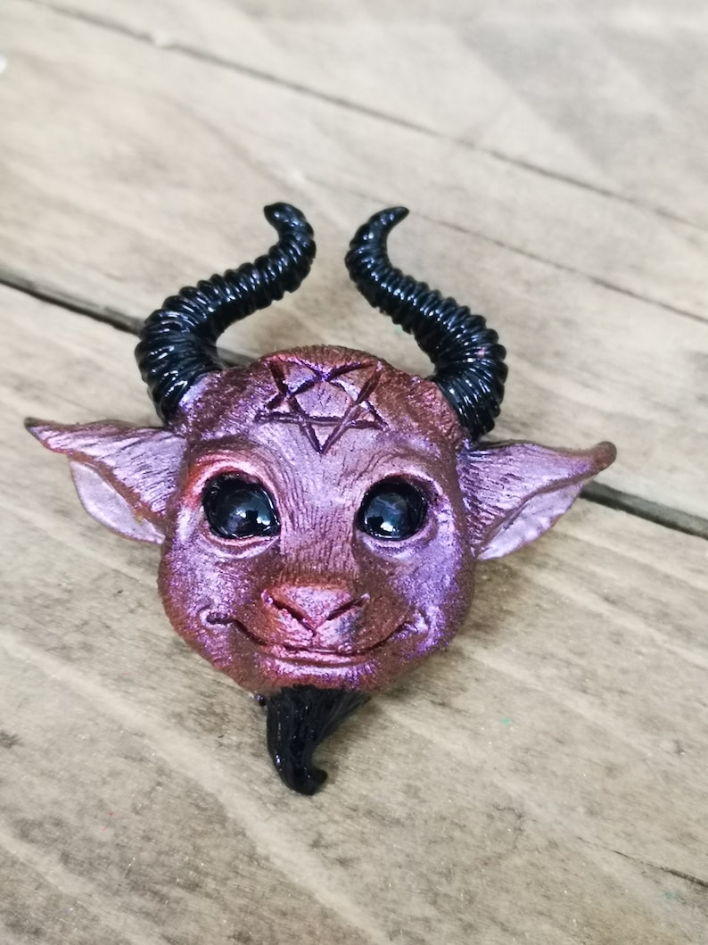 Puede incluir: Una peque&ntilde;a figurita esculpida de un demonio, de color morado y negro, con cuernos, un pentagrama en la frente y una peque&ntilde;a barba.
