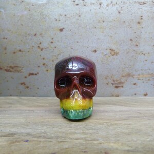 May include: A small, colourful resin skull with a red, yellow and green paint scheme. The skull has black eye sockets and a detailed, sculpted face.