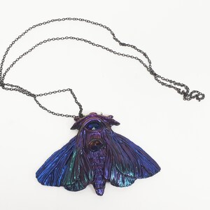 May include: A iridescent blue and purple moth pendant necklace with a black chain. The moth has a large eye on its head and intricate details on its wings.