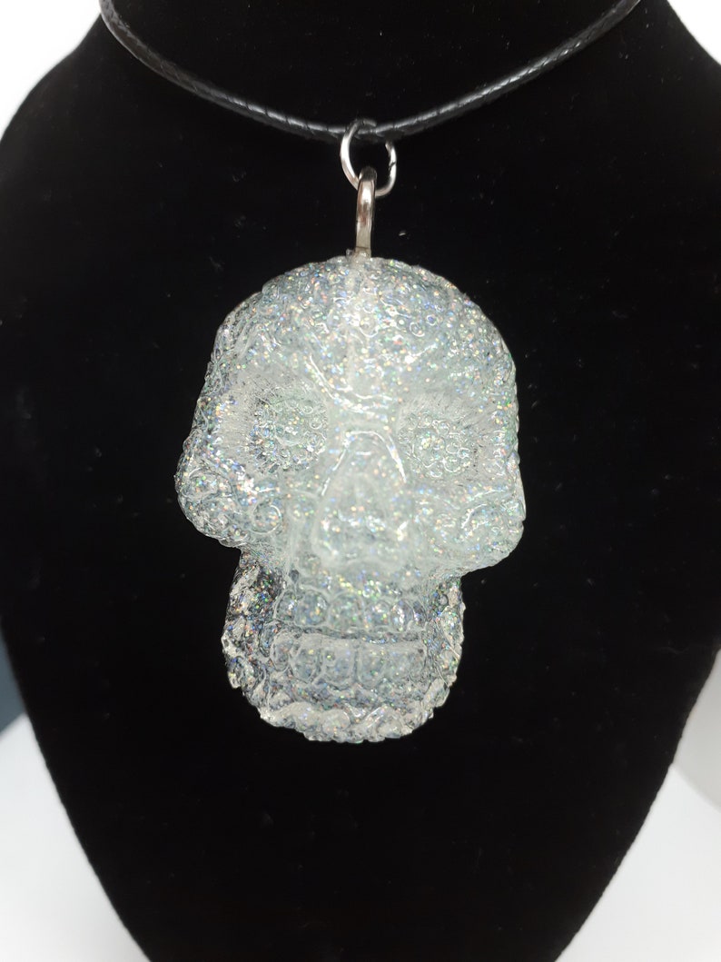 May include: A silver glitter skull pendant necklace with a black cord.