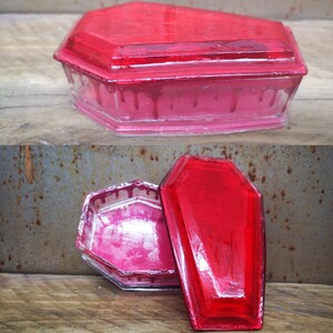 May include: A red glass coffin-shaped trinket box with a dripping blood effect. The box is open and the lid is sitting next to it.