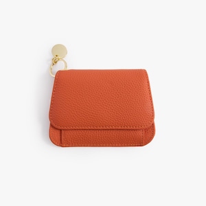 May include: A small, orange leather wallet with a gold key ring attached. The wallet has a fold-over flap and a textured surface.