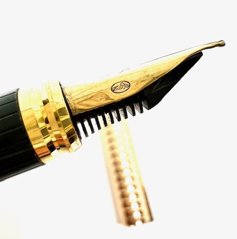 Puede incluir: Primer plano de una plumilla de pluma estilogr&aacute;fica dorada con un cartucho de tinta negro. La plumilla tiene un dise&ntilde;o decorativo y las palabras "G.E.S.A." est&aacute;n grabadas en el lateral.