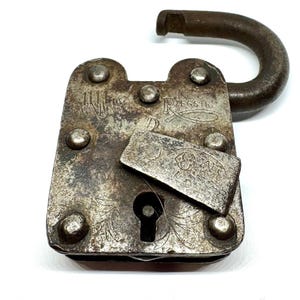 May include: An antique, open padlock with a weathered, silver-toned finish. The lock features a rectangular body with rounded edges, rivets, and an arched shackle. The surface shows engraved floral patterns and the word "REGSTR".
