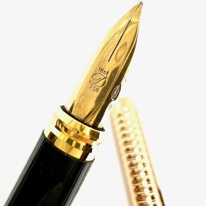 Puede incluir: Primer plano de una pluma de fuente chapada en oro con cuerpo negro y dorado. La pluma est&aacute; grabada con "18ct 750".