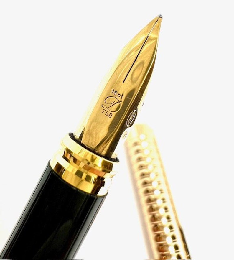 Puede incluir: Primer plano de una pluma de fuente chapada en oro con cuerpo negro y dorado. La pluma est&aacute; grabada con "18ct 750".