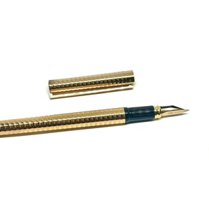 Puede incluir: Una pluma estilogr&aacute;fica dorada con un cartucho de tinta negro y una tapa dorada a juego. La pluma tiene un dise&ntilde;o texturizado y acanalado.