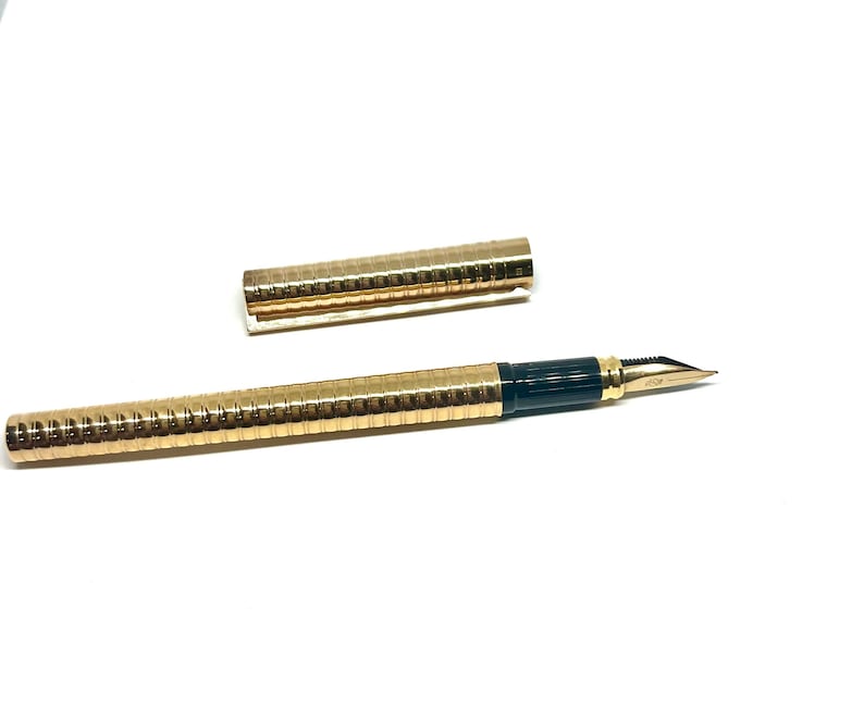 Puede incluir: Una pluma estilogr&aacute;fica dorada con un cartucho de tinta negro y una tapa dorada a juego. La pluma tiene un dise&ntilde;o texturizado y acanalado.