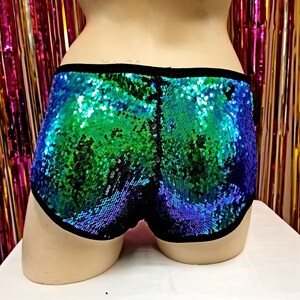 May include: Sequin shorts in shades of blue and green, with a black trim. The shorts are covered in shimmering sequins, creating a vibrant and eye-catching effect. The garment is displayed on a mannequin.