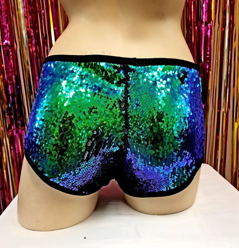 May include: Sequin shorts in shades of blue and green, with a black trim. The shorts are covered in shimmering sequins, creating a vibrant and eye-catching effect. The garment is displayed on a mannequin.