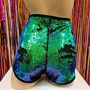 May include: Sequin shorts in shades of green and blue, with a black trim. The shorts are covered in iridescent sequins, creating a shimmering effect. The shorts are displayed on a mannequin.
