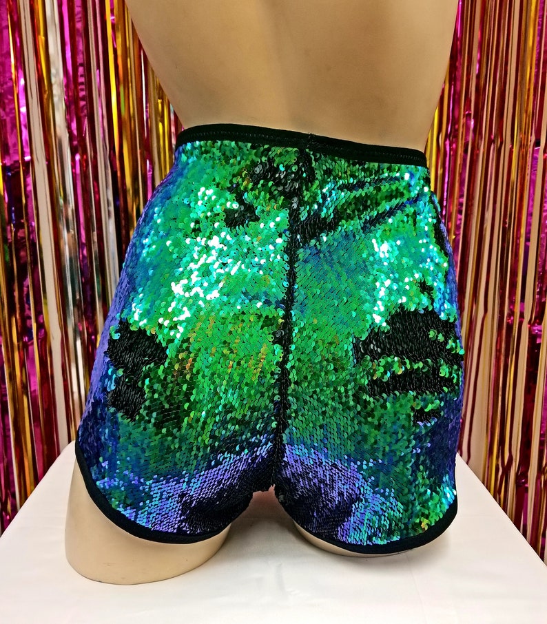 May include: Sequin shorts in shades of green and blue, with a black trim. The shorts are covered in iridescent sequins, creating a shimmering effect. The shorts are displayed on a mannequin.