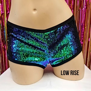 May include: Low-rise shorts with iridescent sequins in shades of green and blue, bordered with black trim. The shorts are displayed on a mannequin. The text "LOW RISE" is printed in black on the mannequin.