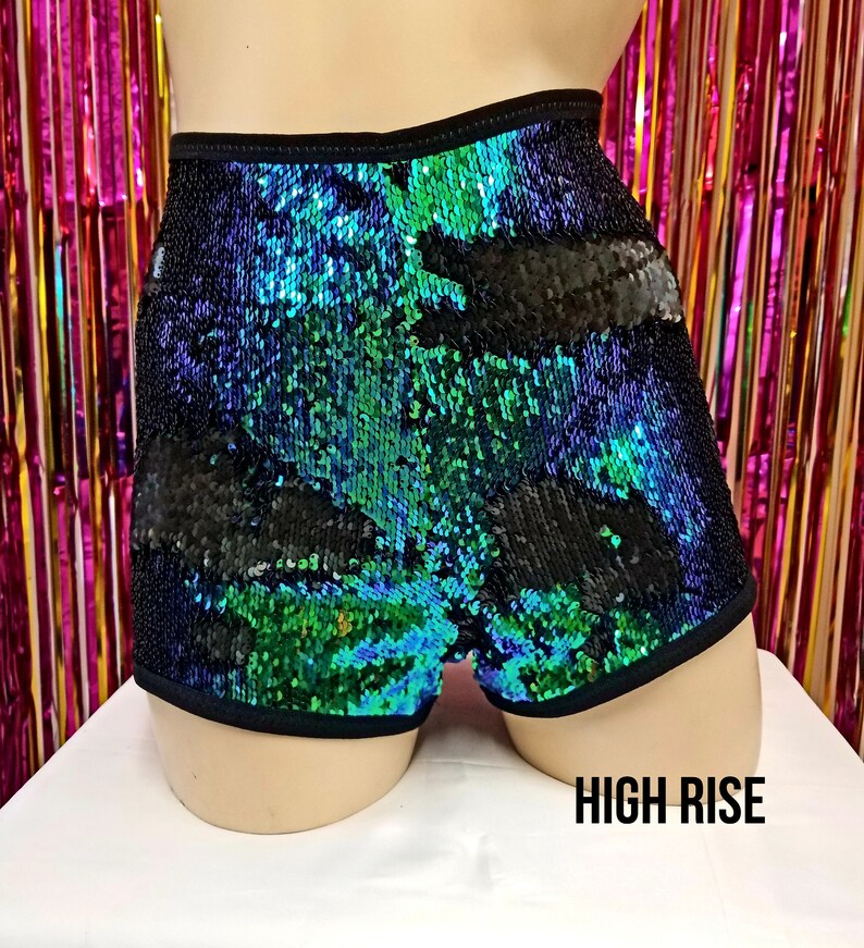 May include: High-waisted shorts covered in iridescent sequins, with a color gradient of green, blue, and black. The shorts have a black elastic waistband and trim. The text "HIGH RISE" is displayed at the bottom.