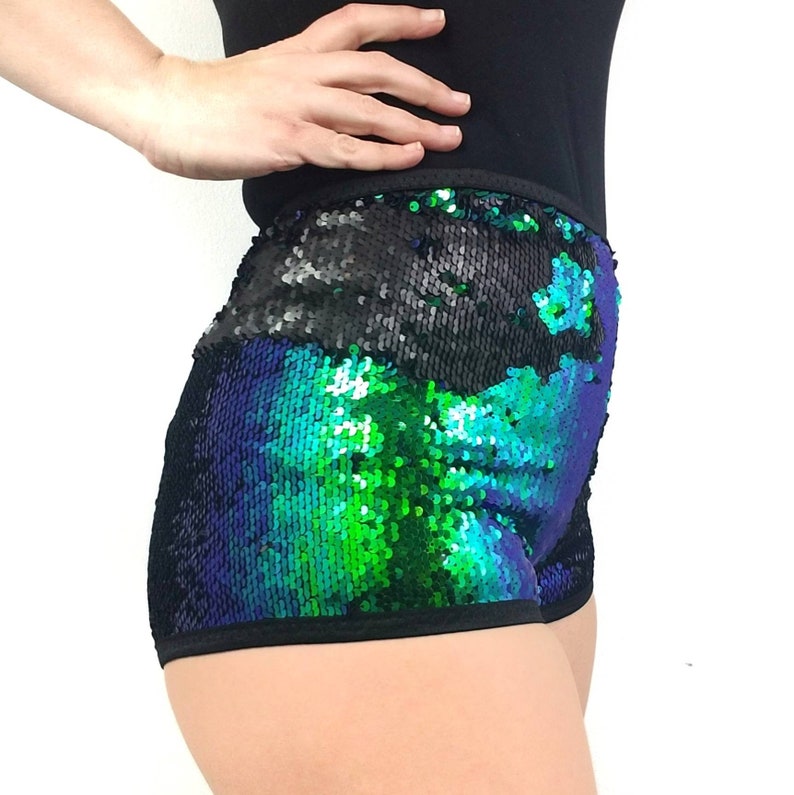 May include: Sequin shorts in a vibrant color scheme of black, green, and blue. The shorts have a black waistband and are covered in shimmering sequins. The garment is designed for dance or performance wear.