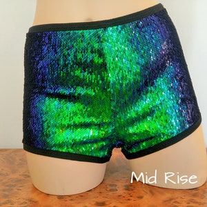 May include: Sequin shorts in a vibrant green and blue color scheme. The shorts have a black trim around the waist and leg openings. The mid-rise design is visible. The sequins create a shimmering effect.