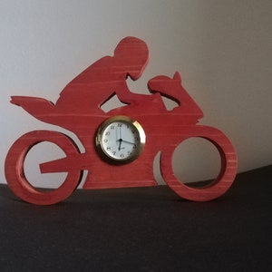 Könnte beinhalten: Rote Holz-Uhr in Form eines Motorrads mit Fahrer. Das Zifferblatt der Uhr ist weiß mit schwarzen Zahlen und Zeigern.