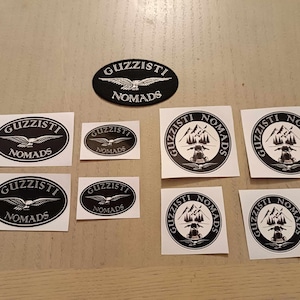 Könnte beinhalten: Neun schwarze und weiße Aufkleber mit dem Text "Guzzisti Nomads" und einer stilisierten Vogel- oder Motorradgrafik.