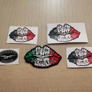 Op de afbeelding: Vijf stickers en een patch met het Guzziisti Nomads logo. Het logo is een gestileerde adelaar met gespreide vleugels, die over een rood-wit-groene Italiaanse vlag vliegt. De stickers zijn gedrukt op wit papier en de patch is geborduurd.