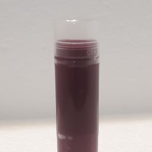 May include: A clear, cylindrical container with a dark purple liquid inside. The container has a white base and a clear, rounded top. The liquid appears to be a deep shade of purple. The top of the container has the text "08A".