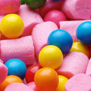 May include: A variety of colorful bubble gum, including pink, red, blue, yellow, and orange, is scattered on a pink surface. The gum is in various shapes and sizes.