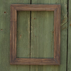 May include: A dark brown wooden picture frame with a simple design, against a backdrop of weathered green wood.