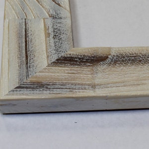 May include: Close-up of a corner of a whitewashed wood picture frame. The frame has a rustic, distressed look with visible wood grain.