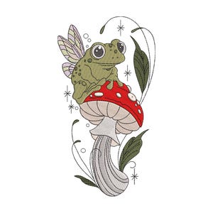 May include: An embroidery design featuring a green frog with light purple fairy wings perched atop a red mushroom with white spots. The design includes thin black line art of leaves, small circles, and starburst accents surrounding the central figures.
