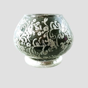 May include: A black ceramic candle holder with a silver floral design. The holder has a round base and a wide, rounded top.