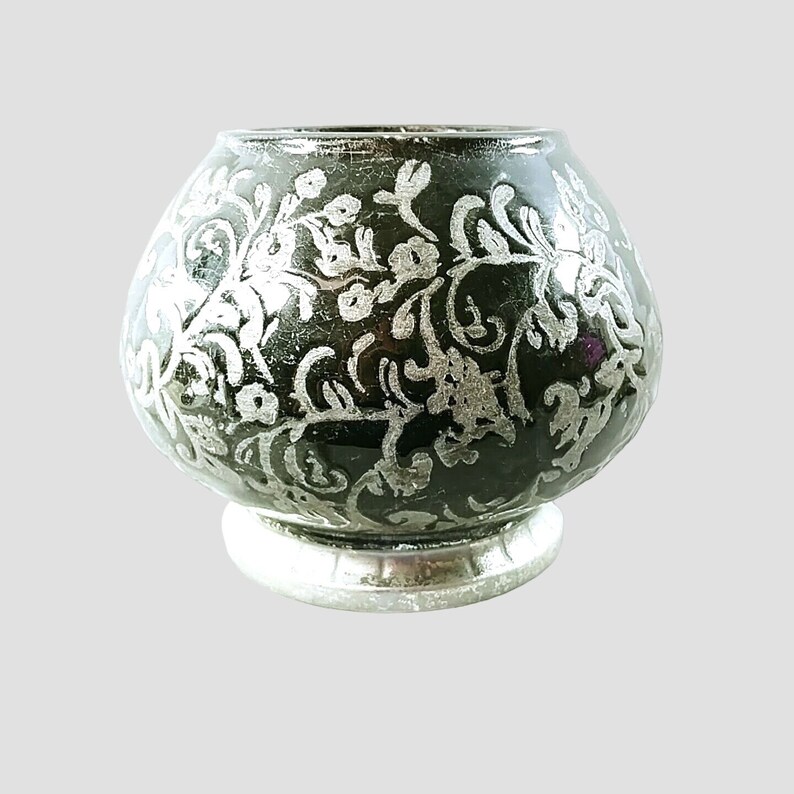 May include: A black ceramic candle holder with a silver floral design. The holder has a round base and a wide, rounded top.