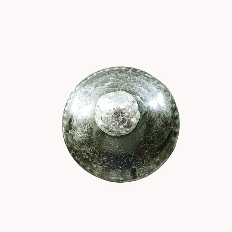 May include: A green ceramic bottle stopper with a silver top. The stopper has a crackled glaze finish.