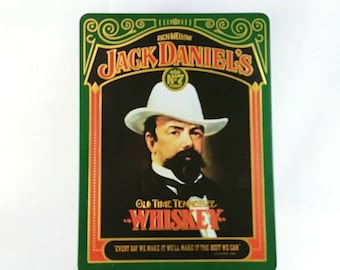 May include: A green and gold tin with a picture of Jack Daniel's, a man in a white hat, and the text "RICH MELLOW JACK DANIEL'S OLD TIME TENNESSEE WHISKEY" and "EVERY DAY WE MAKE IT, WE'LL MAKE IT THE BEST WE CAN."