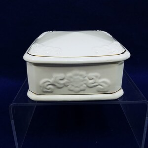 May include: A white porcelain trinket box with a gold trim and an embossed floral design.