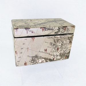 May include: A rectangular box with a vintage map design on the front and top. The map is in shades of brown, beige, and red. The box is made of wood and has a black trim.