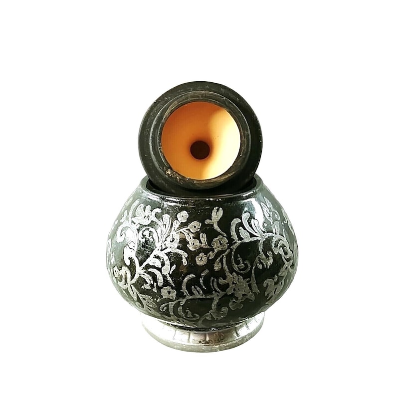 May include: A black ceramic pot with a silver floral design. The pot has a round shape and a lid with a small opening in the center.
