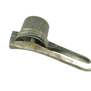 May include: A vintage metal potato ricer with a green handle. The ricer is made of metal and has a mesh design. It is used to mash potatoes.