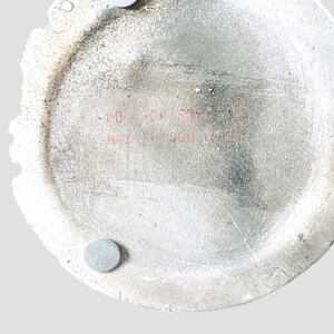 May include: A white ceramic plate with a round shape and a slightly raised edge. The plate has a textured surface and a small, round, silver sticker on the bottom. The plate has red text that reads "NOT FOR STOVES" and "MAY BE DAMAGED BY HEAT".