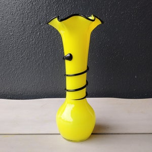 May include: A yellow glass vase with a black swirl design. The vase has a wide mouth and a narrow base.