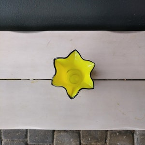 May include: A yellow glass vase with a star-shaped opening and black trim.