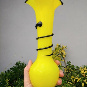 May include: A bright yellow glass vase with a black swirl design. The vase has a wide mouth and a rounded bottom.