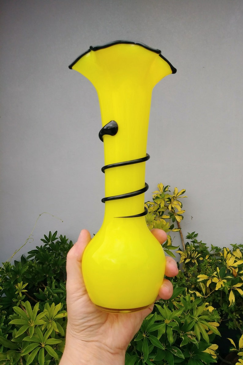 May include: A bright yellow glass vase with a black swirl design. The vase has a wide mouth and a rounded bottom.