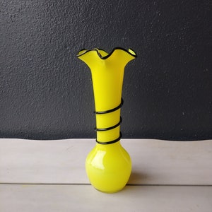 May include: A bright yellow glass vase with a black swirl design and a ruffled top.